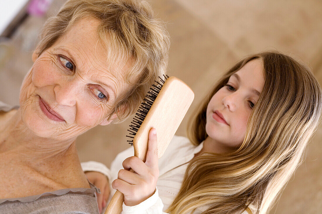 Little girl brushing senior woman's hair, indoors