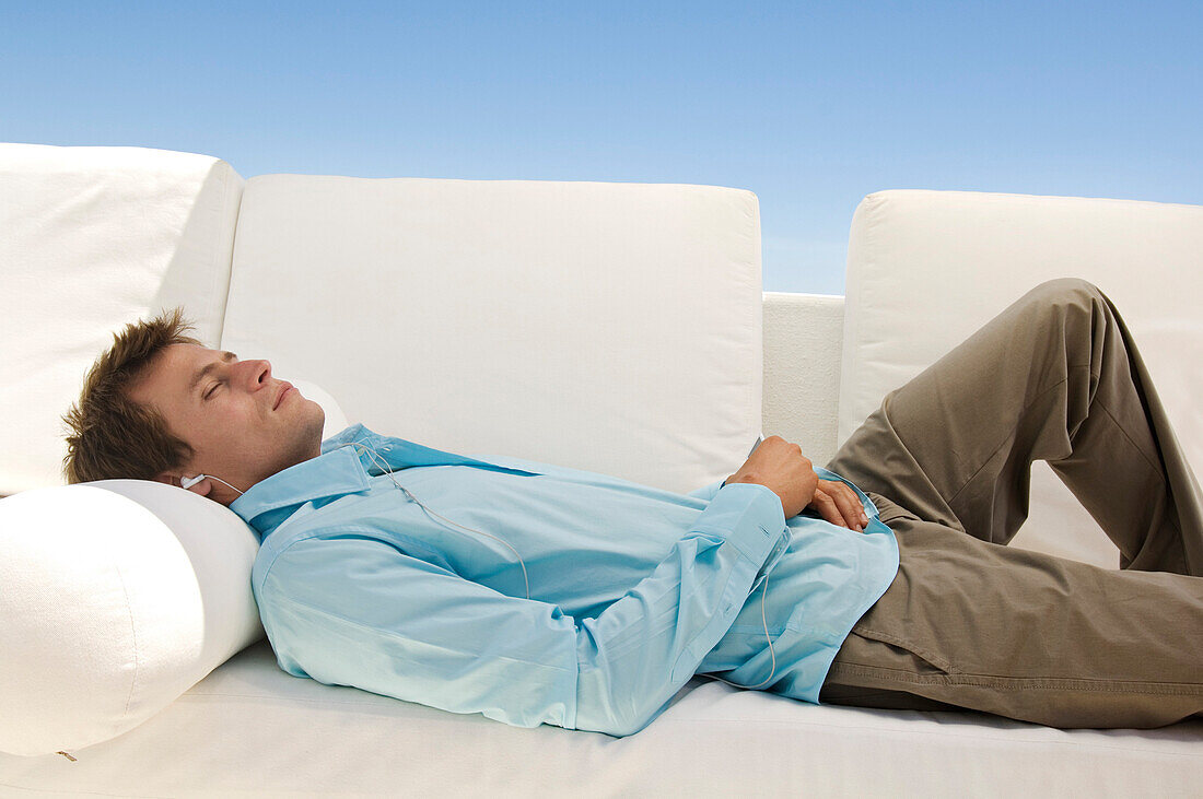 Young man listening to MP3 player lying on sofa