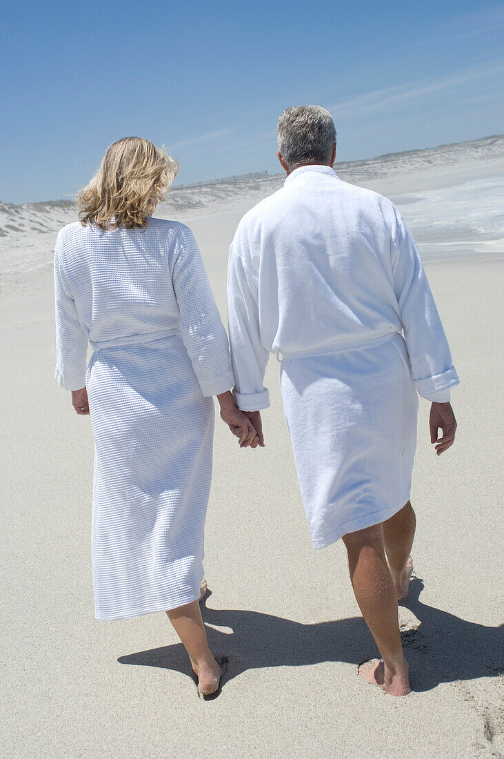 Couple in bathrobe walking on the beach, rear view
