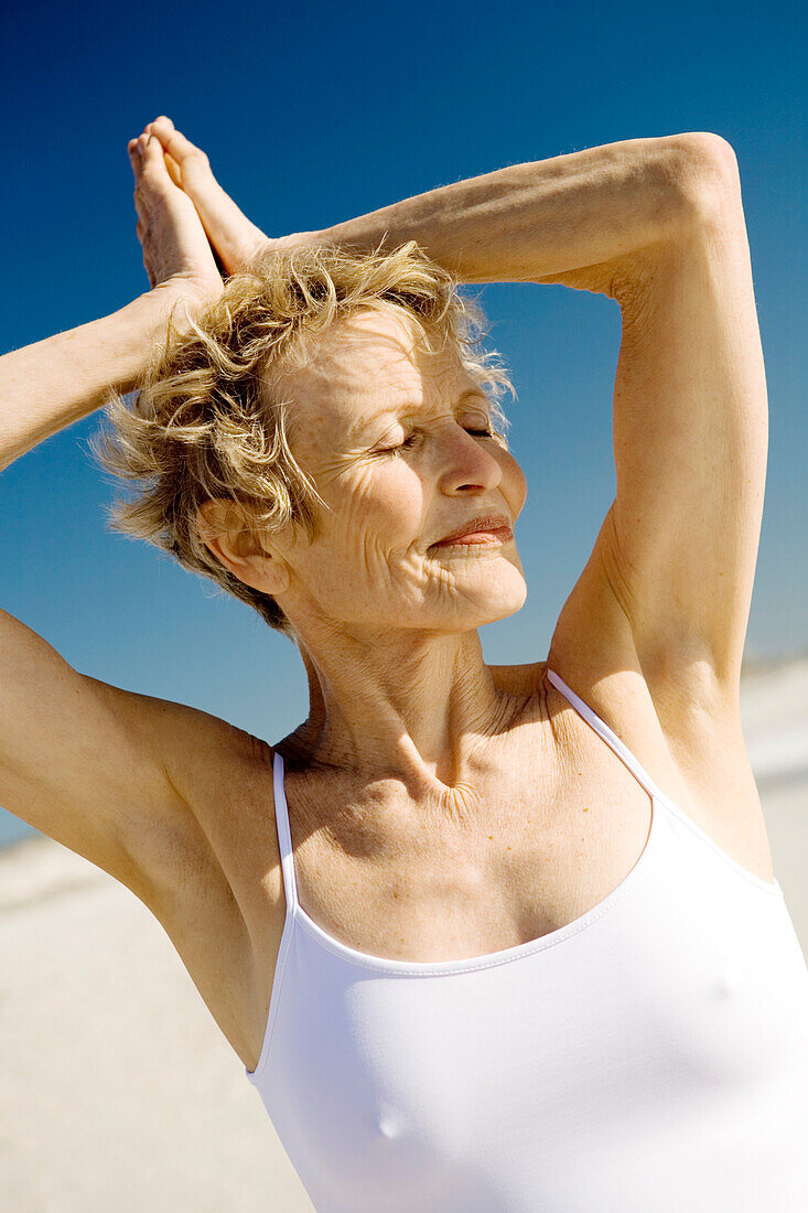 Senior woman doing yoga on the beach