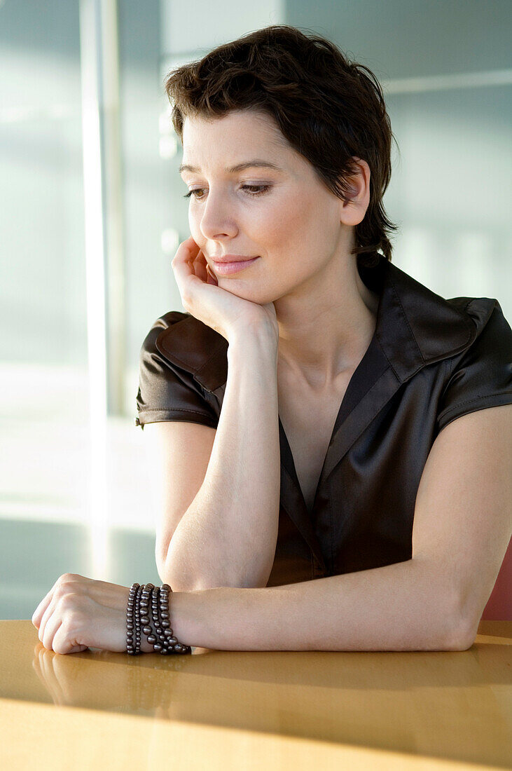 Close-up of a mid adult woman sitting at a table with her hand on her chin