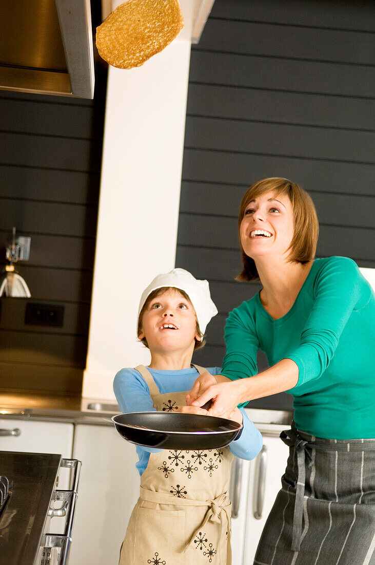 Young woman flipping a pancake with her son