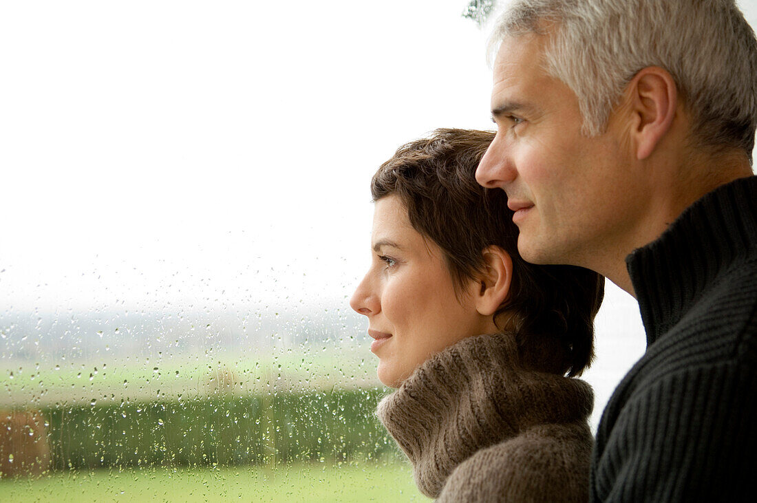 Mature man and a mid adult woman looking out through a window