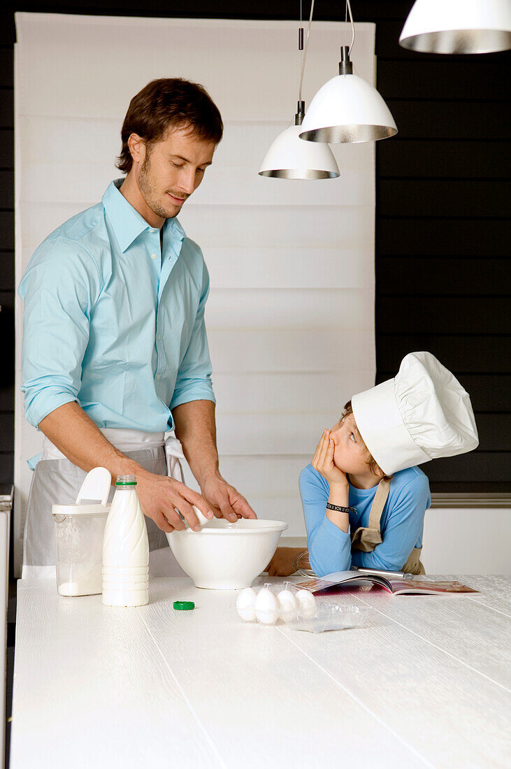 Mid adult man making a cake and his son in the kitchen