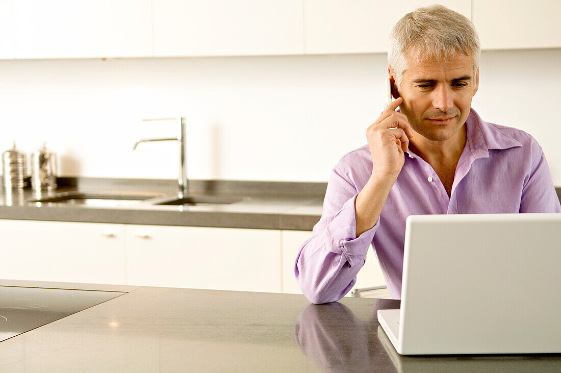 Mature man working on a laptop while talking on a mobile phone