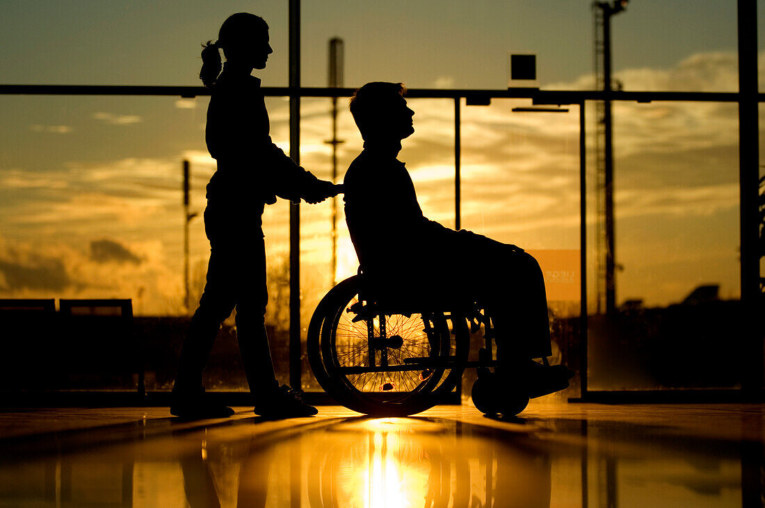 Silhouette of a woman pushing a male patient sitting in a wheelchair