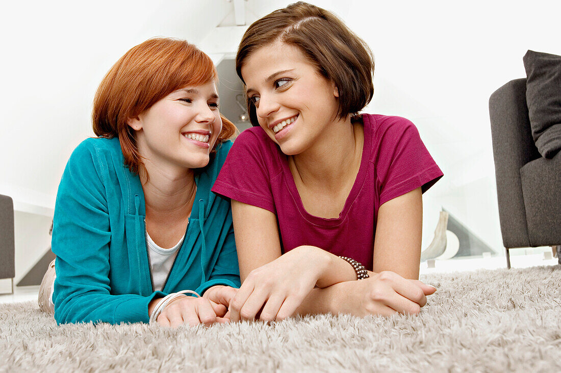 Close-up of two young women lying on a carpet and smiling