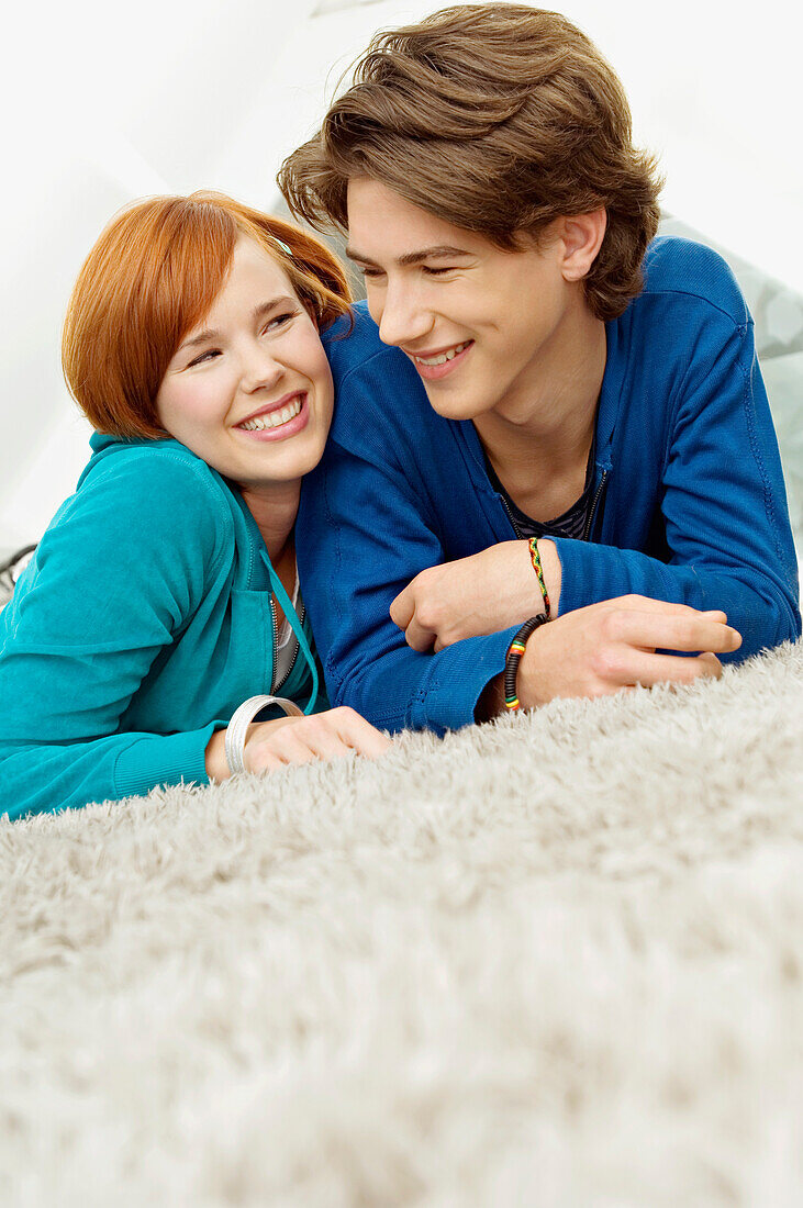 Close-up of a young woman with a teenage boy lying on a carpet and smiling