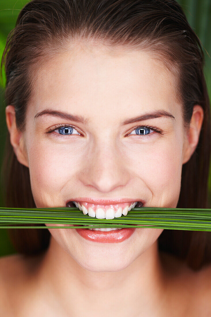 Young smiling woman holding plants between teeth