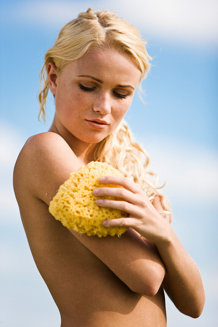 Naked young woman holding a wet bath sponge