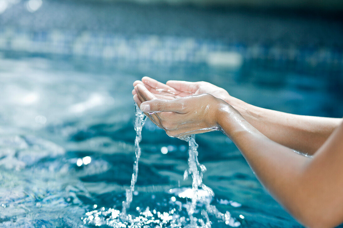 Wasser tropft aus den schalenförmigen Händen einer Frau
