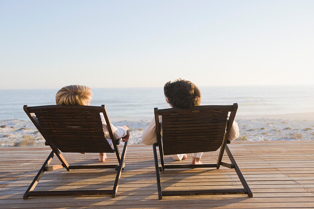 Couple reclining on deck chairs on the beach
