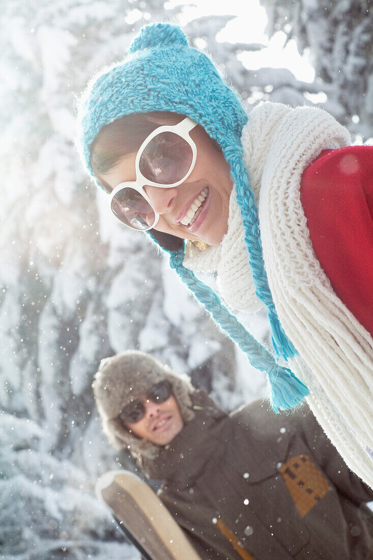 Young woman in winter clothes smiling at camera, man holding skis in background