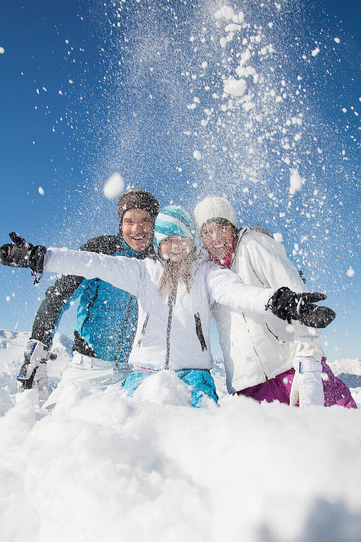 Couple and daughter in ski wear, throwing snow in air