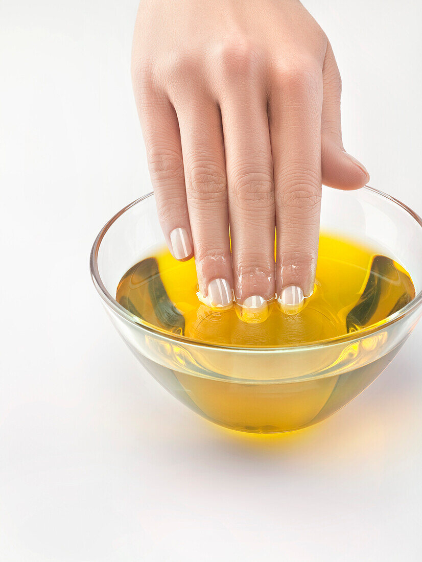 Nahaufnahme einer Frauenhand in einer Schale mit Olivenöl