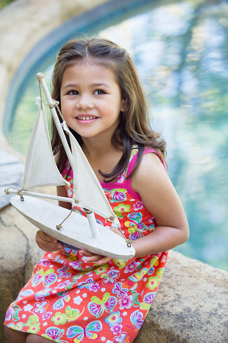 Little girl sitting by the swimming pool with model of boat in hand
