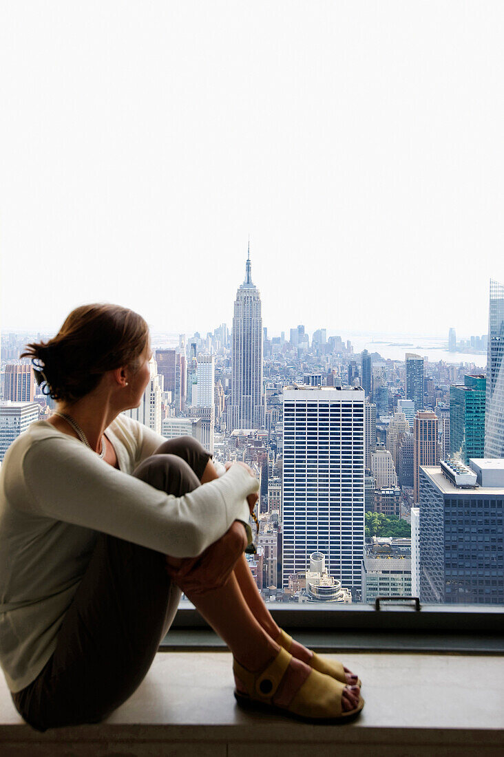 Frau sitzt auf einer Fensterbank und betrachtet Empire State Building, Rockefeller Center, Manhattan, New York City, New York, USA