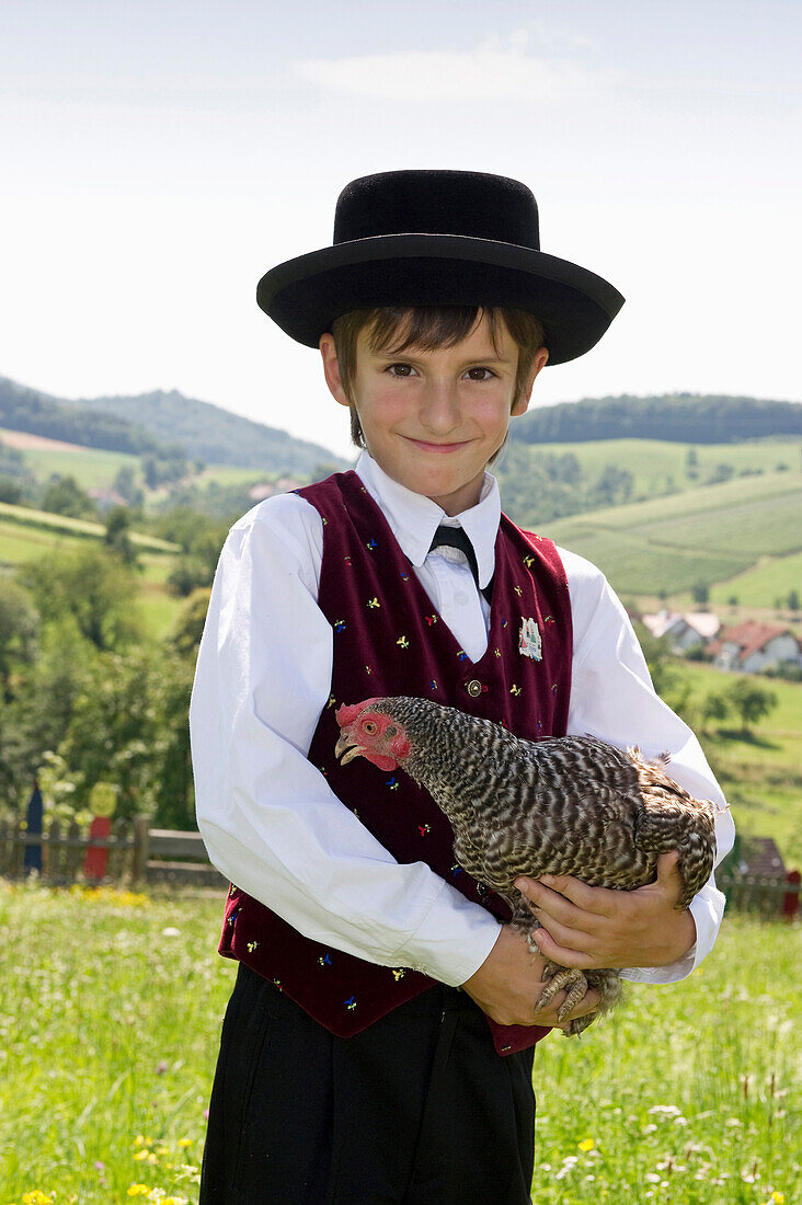 Boy holding a chicken wearing traditional Black Forest clothes, Gottertal, Baden-Wurttemberg, Germany