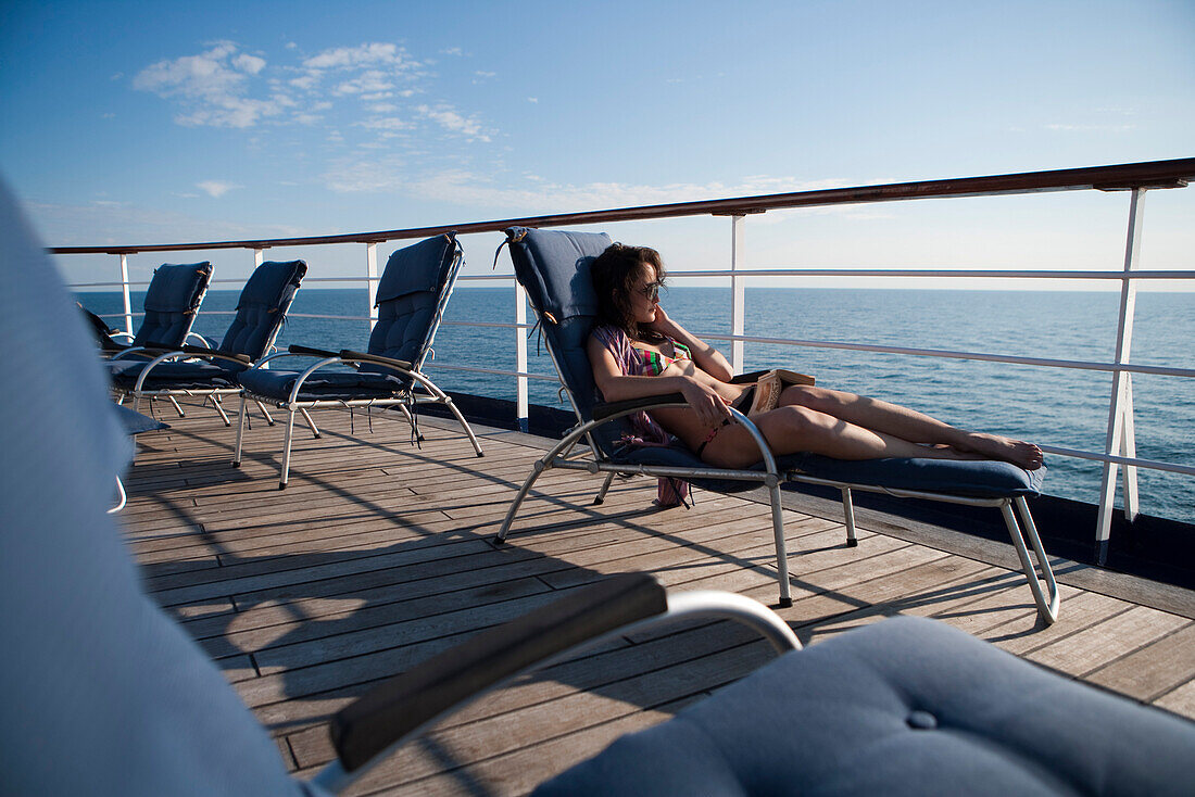 Frau enstpannt sich auf Liegestuhl an Deck von Kreuzfahrtschiff MS Astor (Transocean Kreuzfahrten) während einer Kreuzfahrt durch die Ostsee, nahe Dänemark, Europa MR