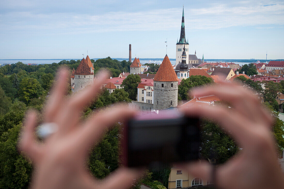 Hands hold compact camera to capture overhead of city with churches and towers from Toompea hill, Tallinn, Harjumaa, Estonia