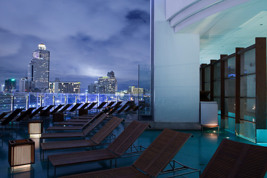 Liegestühle und Schwimmbad im Millennium Hilton Hotel mit Blick auf Skyline bei Nacht, Bangkok, Thailand, Asien