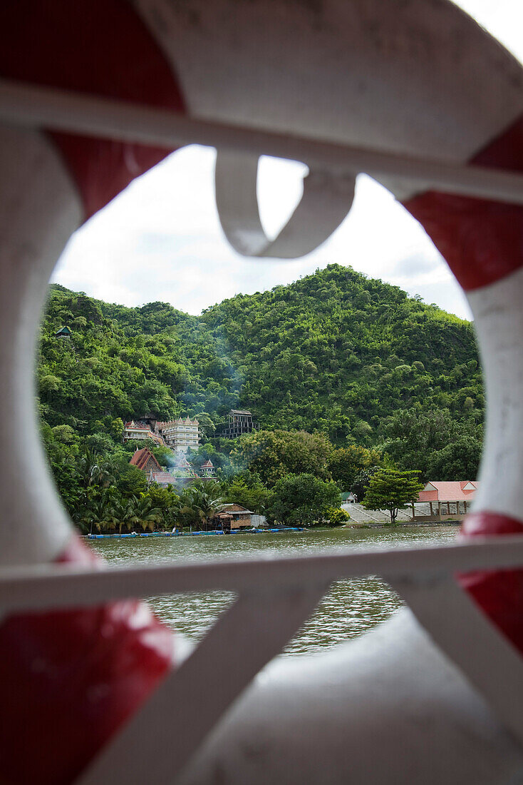 Chinesischer Tempel mit Aufgang in Form von Drachen, Blick durch Rettungsring von Flusskreuzfahrtschiff RV River Kwai während einer Kreuzfahrt auf dem Fluss River Kwai Noi, nahe Kanchanaburi, Thailand, Asien