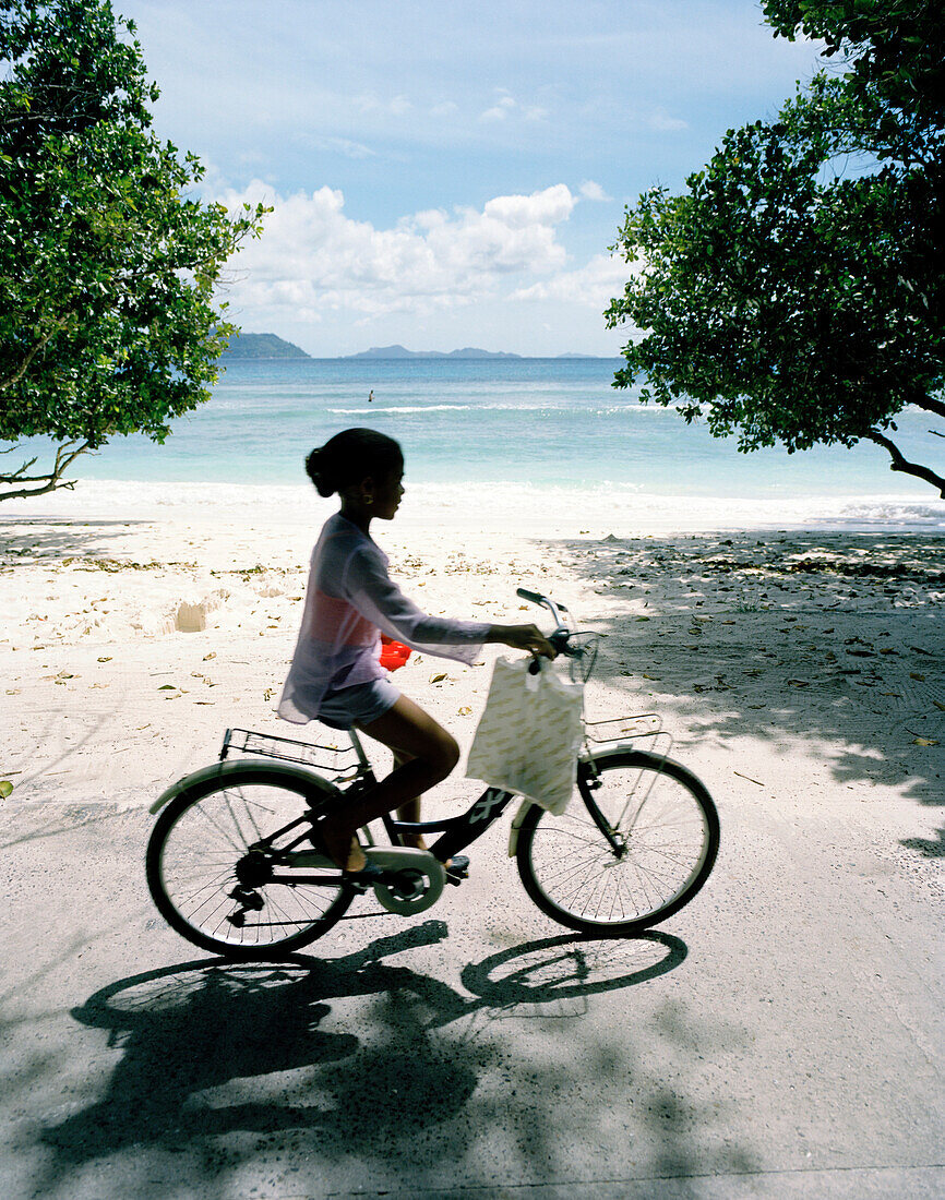 Radfahrerin am Strand Anse Severe, nördwestliches La Digue, La Digue and Inner Islands, Republik Seychellen, Indischer Ozean