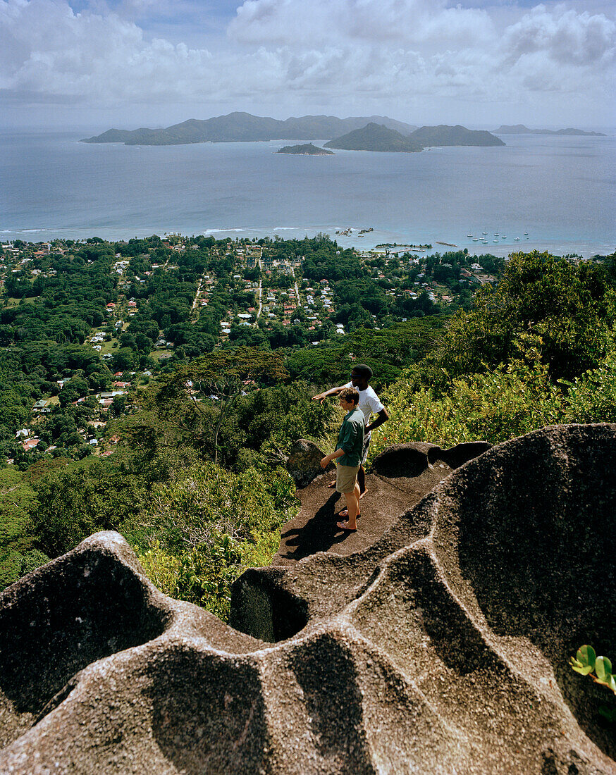 Wanderer auf Granitfelsen auf dem Weg zum Aussichtspunkt Nid d'Aigles auf über 300 m, Blick über Dorf La Passe bis Nachbarinsel Praslin, inneres La Digue, La Digue and Inner Islands, Republik Seychellen, Indischer Ozean