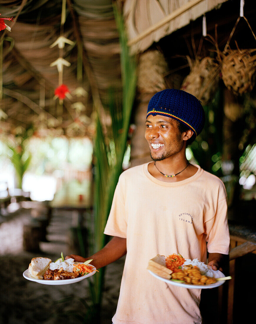 Waiter at restaurant Loutier Coco on Grand Anse beach, south eastern La Digue, La Digue and Inner Islands, Republic of Seychelles, Indian Ocean