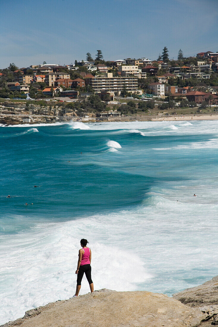 Woman standing on rock over looking Mackensies and Tamarama Bay, near Bondi Beach, Sydney, New South Wales, Australia