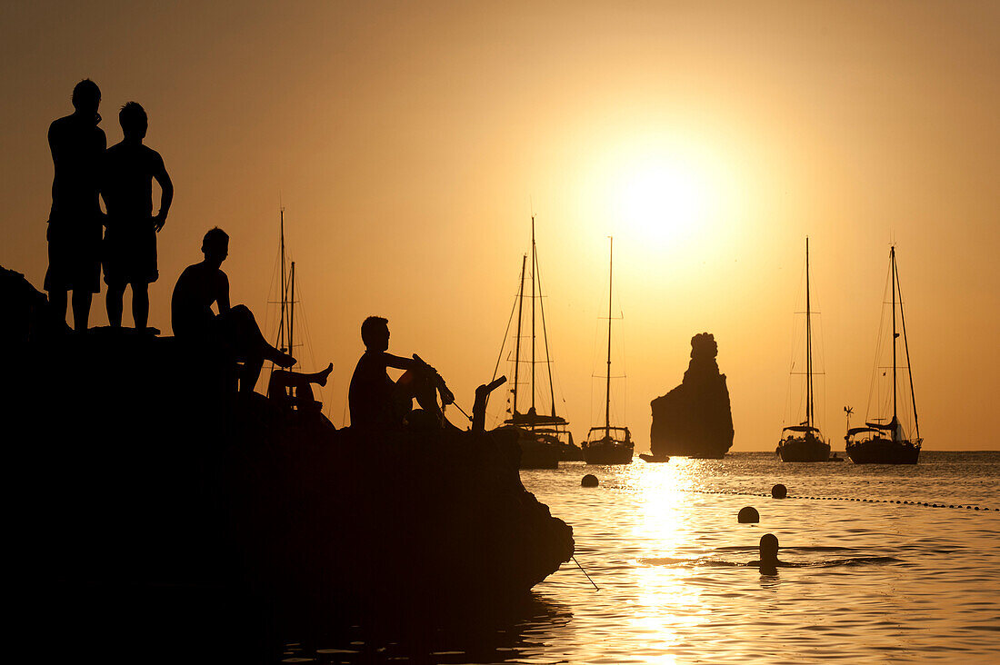 People watching the sunset on rocks beside Benirras beach, Ibiza, Spain.