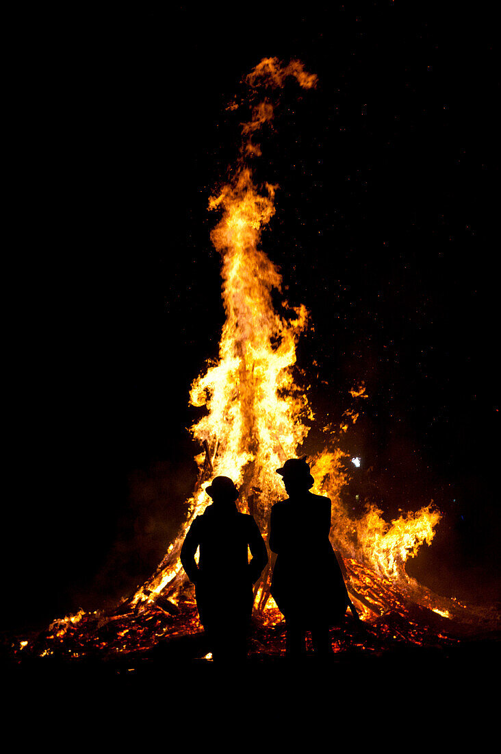 Silhouette of man and woman in front of large bonfire at Battle Bonfire night, East Sussex, England.
