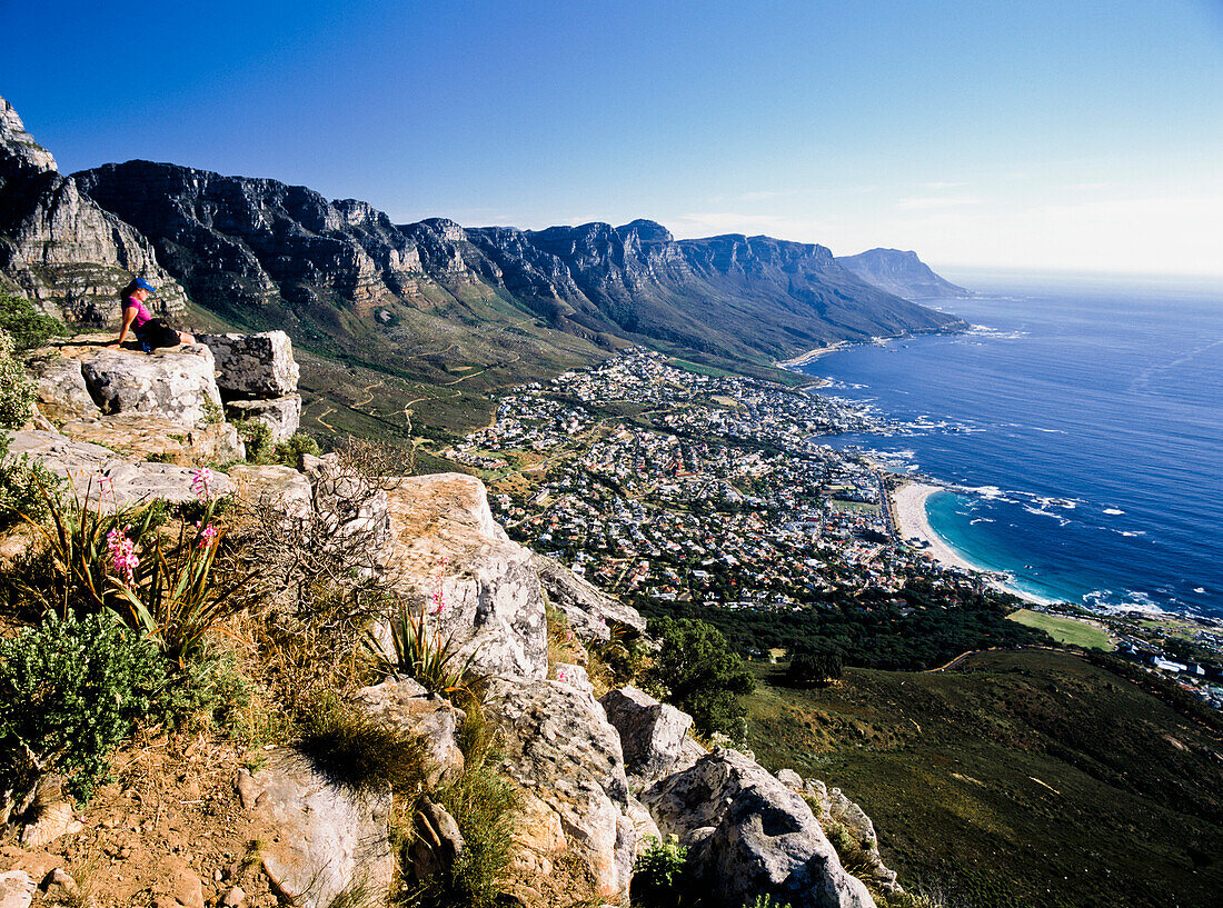 Hiker looking at Camps bay, sitting on top of hill, side view, Capetown, South Africa