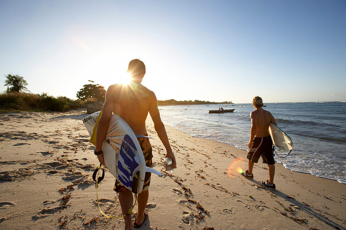 Surfers carrying surfboards on beach, Tanzania