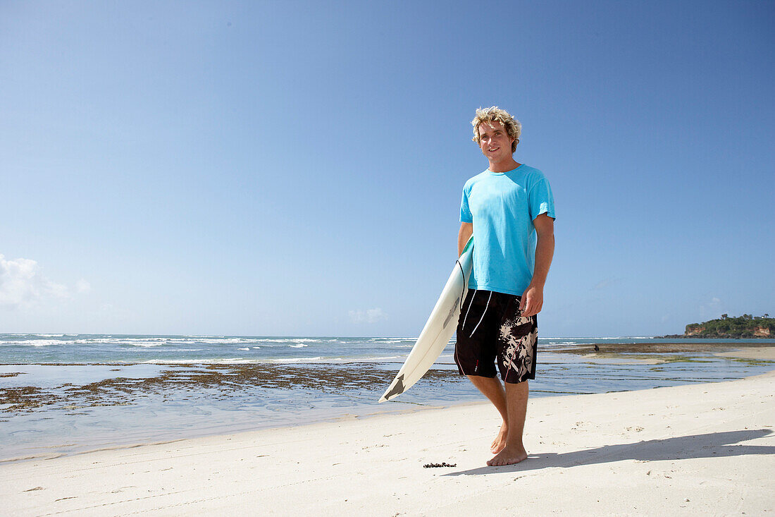 Blond surfer walking on beach with surfboard, Tanzania