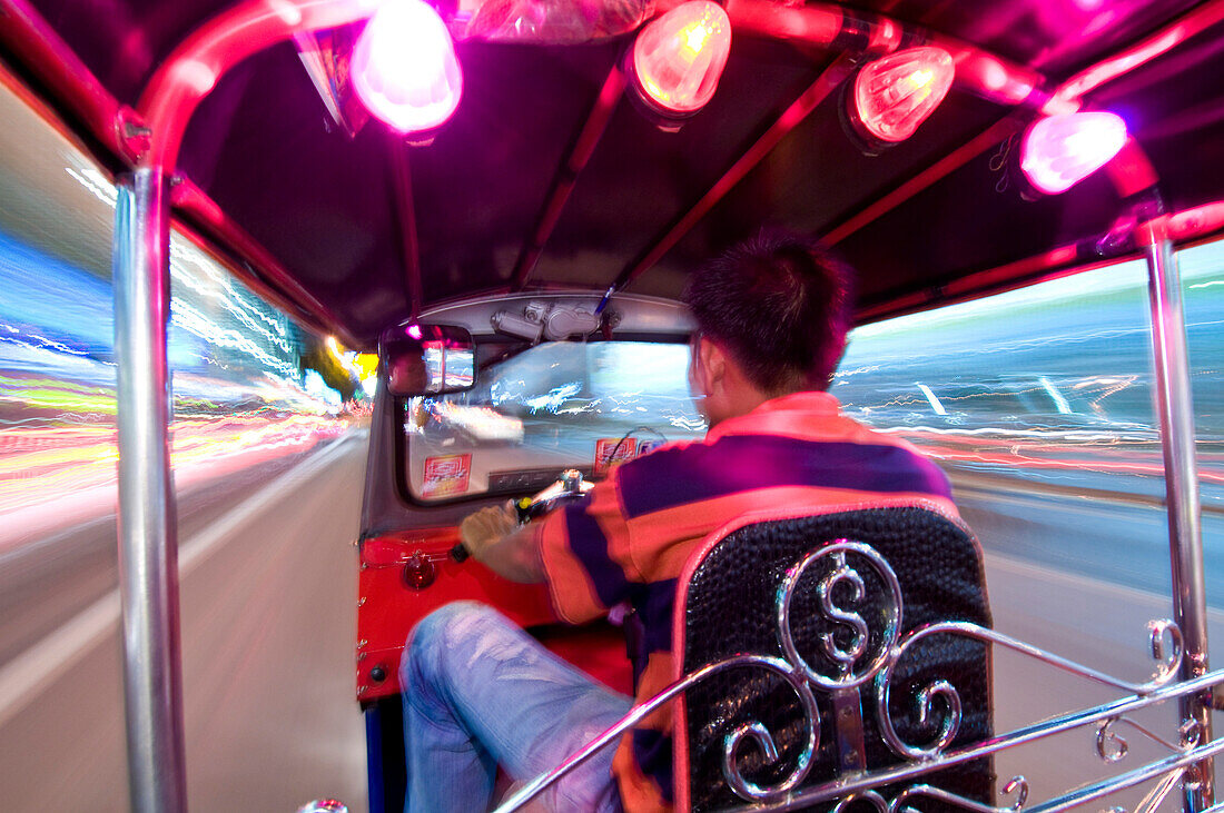 Man driving tuk-tuk at night, Bangkok, Thailand.