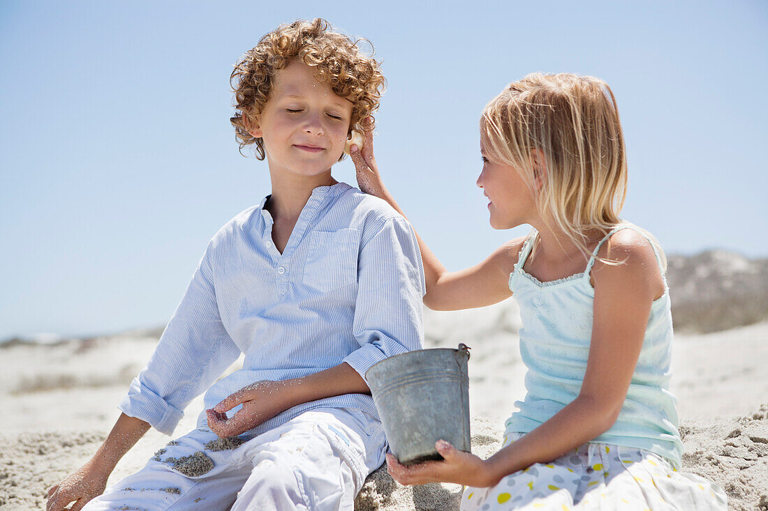 Girl holding shell to her brother's ear on beach