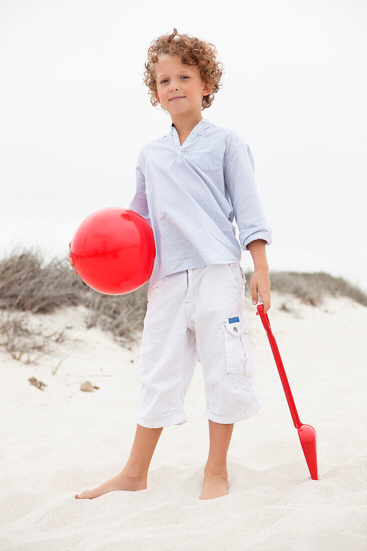 Boy holding toy shovel and ball on beach