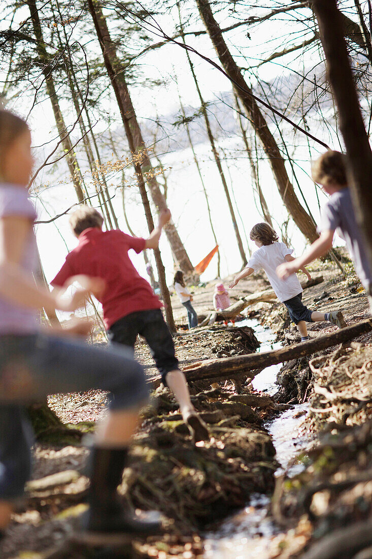 Kinder toben am Seeufer und springen über einen Bach, Schlosspark Leoni, Leoni, Starnberger See, Bayern Deutschland
