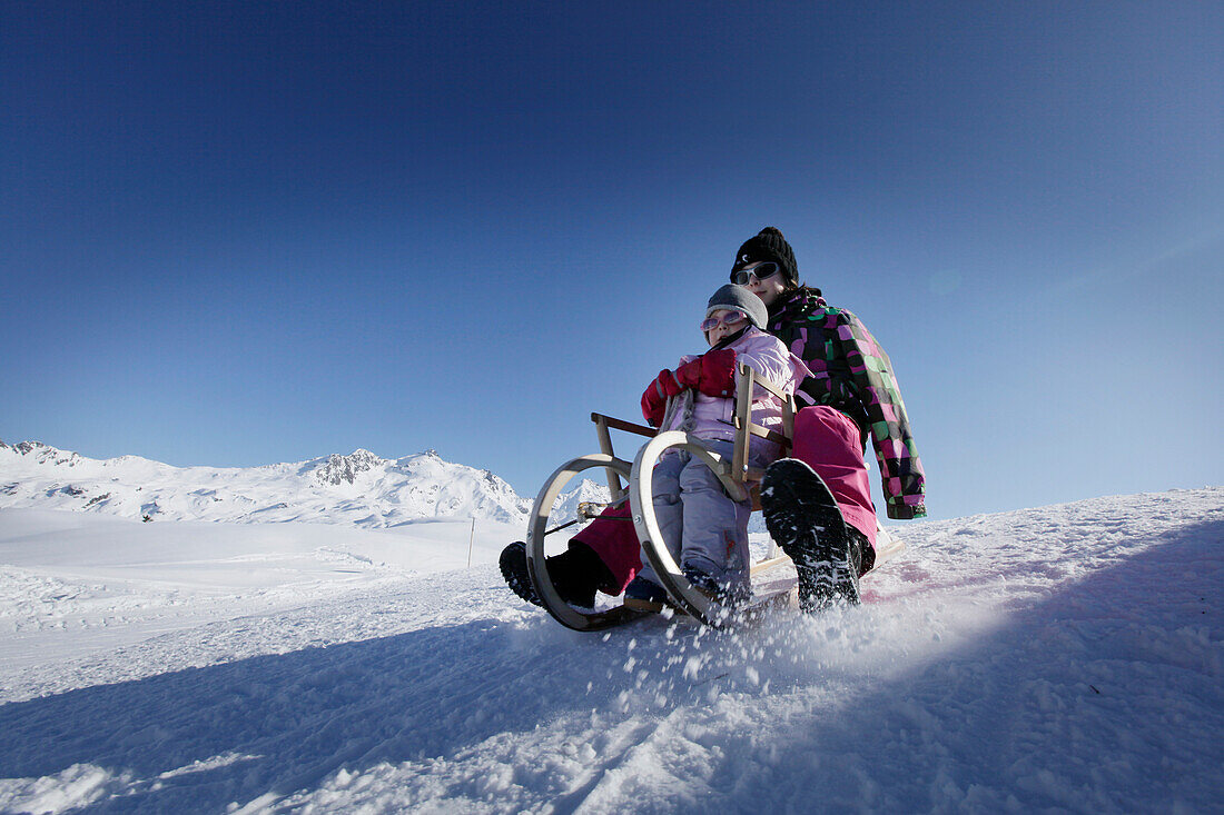 Two girls, 12 and 2 years, sledging down a hill on a tobogan, sledge, Kloesterle, Arlberg, Austria