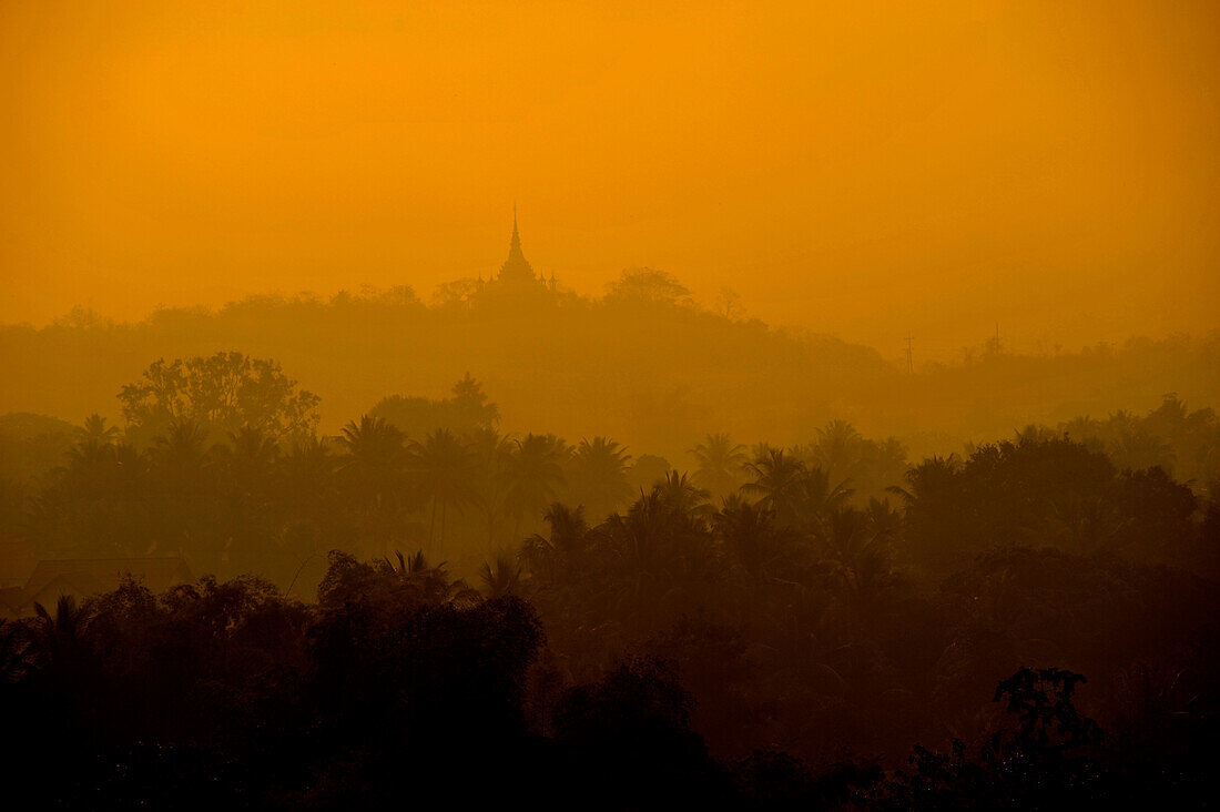 View to the East over trees and hills with pagoda in morning dust, from Phu Si hill, Luang Prabang, Laos