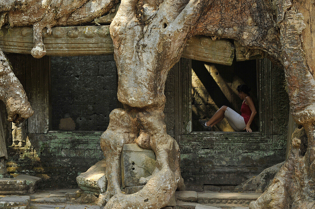 Mächtige Wurzeln an der Galerie in Preah Khan mit einer jungen Frau in einem Fenster, Angkor, Kambodscha, Asien