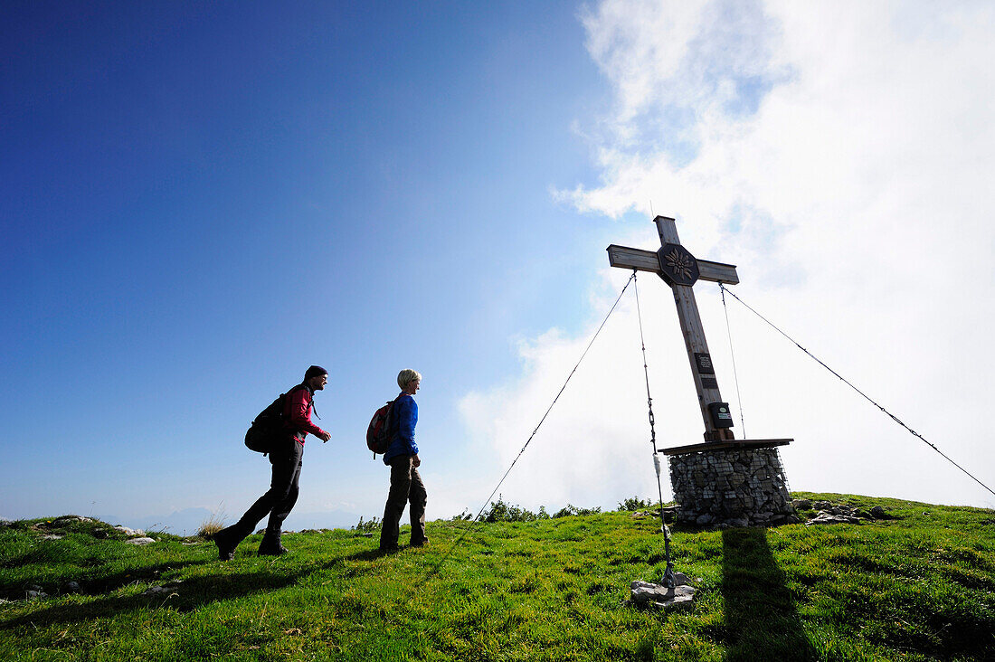 Two hikers walking towards cross at summit, Vorderes Sonnwendjoch, Rofan range, Brandenberg Alps, Tyrol, Austria