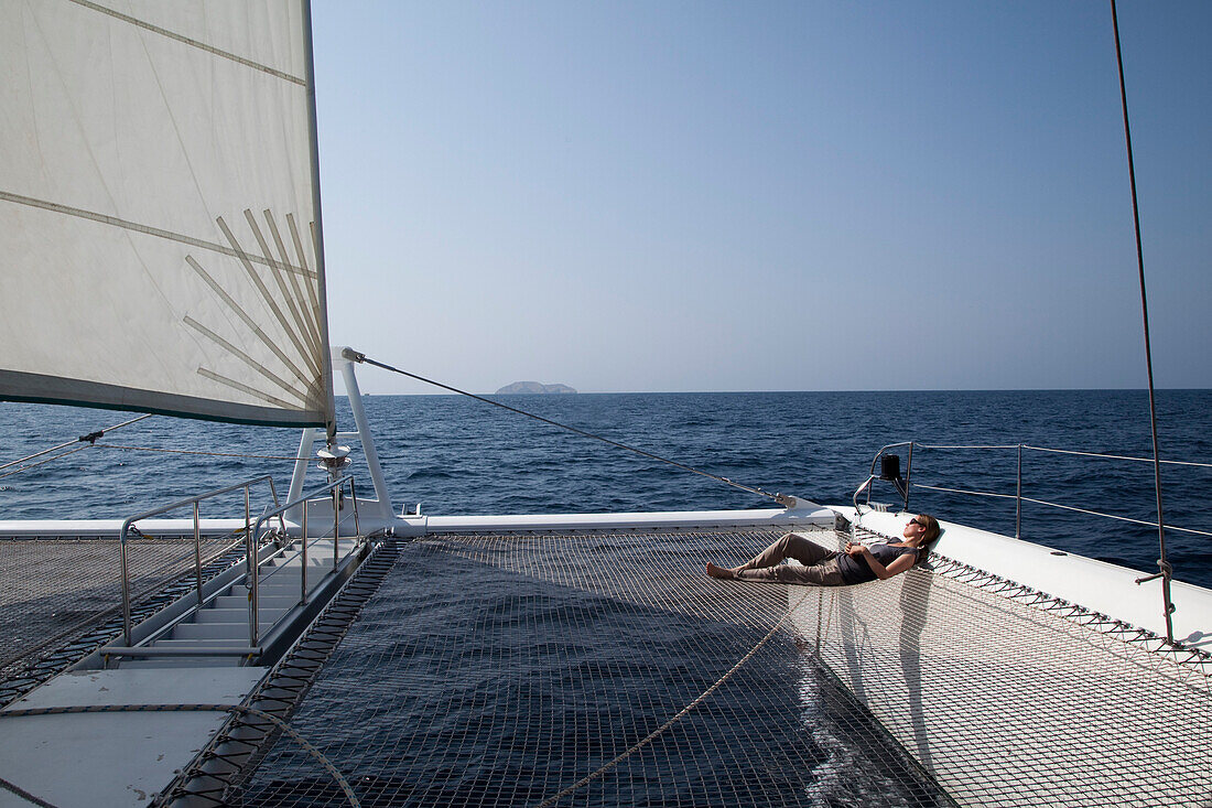 Eine junge Frau entspannt sich im Netz an Bord vom Katamaran SY Azzura, Ocean Blue Oman cruises, nahe Muscat, Maskat, Oman, Arabische Halbinsel