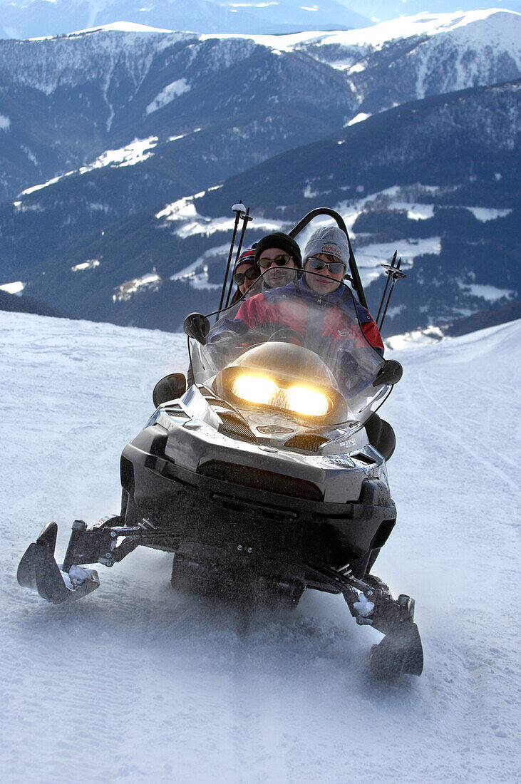 Drei Personen auf einem Schneemobil in den Bergen, Alto Adige, Südtirol, Italien, Europa