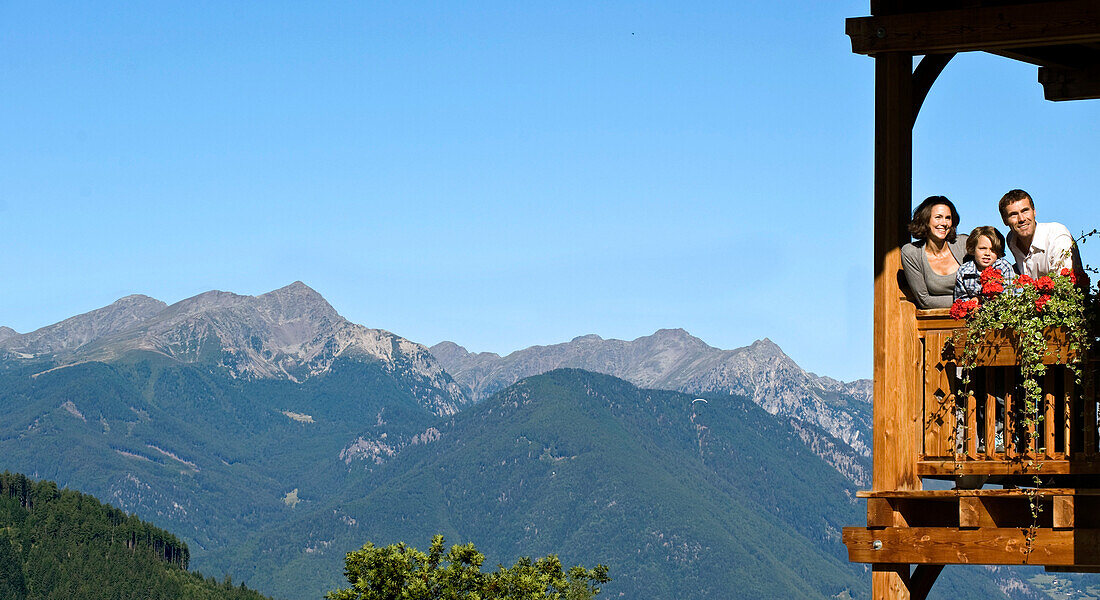 Familie auf einem Balkon vor Bergkette im Sonnenlicht, Lüsen, Alto Adige, Südtirol, Italien, Europa