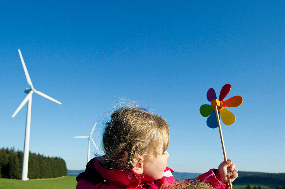 Little girl with toy windmill, wind turbine in the background, Black Forest, Baden-Wurttemberg, Germany