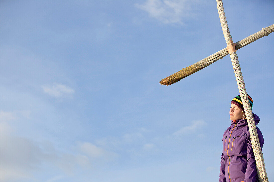 Young woman standing at a cross on a summit in the mountains, See, Tyrol, Austria