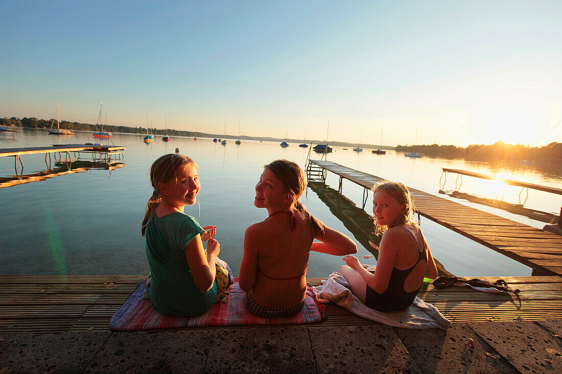 Children sitting on a wooden jetty at sunset, Lake Woerthsee, Starnberg, Upper Bavaria, Bavaria, Germany