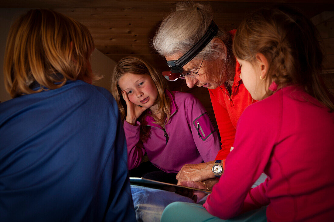 Eine Grossmutter liest drei Kindern, zwei Mädchen und einem Jungen eine Gutenachtgeschichte vor, in einer Berghütte, Schweiz